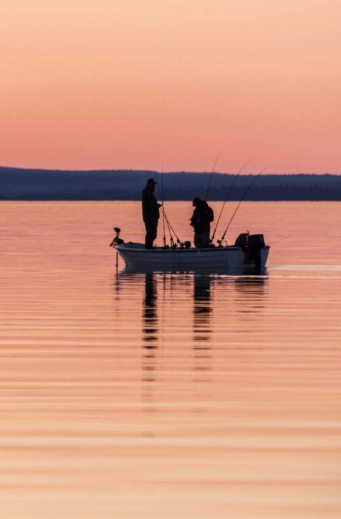 Two people are fishing from a small boat at sunset.